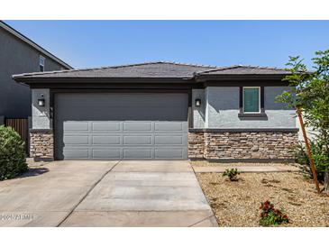 Charming home featuring a grey garage door, stone accents, and low-maintenance landscaping at 17320 W Daley Ln, Surprise, AZ 85387