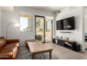 Bright living room featuring a leather sofa, hardwood floors, and a sliding glass door to the balcony at 7300 E Earll Dr # 1022, Scottsdale, AZ 85251