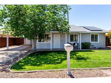 Charming single-story home with a lush green lawn, mature shade tree, and solar panels on the roof at 14008 N 61St Ave, Glendale, AZ 85306