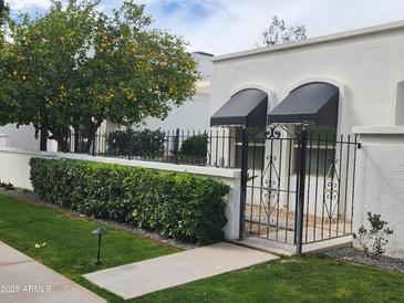 Charming white home with a lush lemon tree, trimmed hedges, and a black wrought iron gate at 4830 N 72Nd Way, Scottsdale, AZ 85251