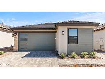 A modern home featuring a gray garage door, neutral stucco and siding and a brick driveway at 20332 W Sells Dr, Buckeye, AZ 85396