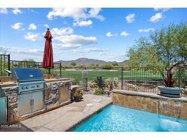 An outdoor kitchen and swimming pool overlook a golf course in this backyard oasis at 1788 W Dion Dr, Anthem, AZ 85086