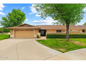 Single-story home featuring an attached two-car garage, manicured lawn and mature trees under a sunny sky at 19053 N Lakeforest Dr, Sun City, AZ 85373