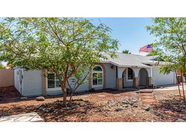 Single-story home with a light blue exterior, desert landscaping, and an American flag in the front yard at 4915 W Libby St, Glendale, AZ 85308