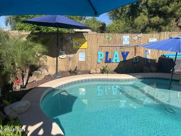 Inviting pool area with vibrant blue water, festive decorations, and tropical landscaping for backyard relaxation and entertainment at 15939 W Post Dr, Surprise, AZ 85374