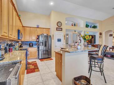Open kitchen with stainless appliances, granite counters, and an eat-in bar, flowing to the dining and living areas at 230 S 122Nd Ln, Avondale, AZ 85323