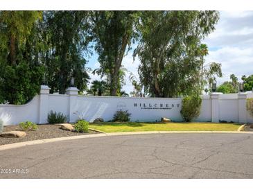 An entrance to the Hillcrest private adult community is defined by a white brick wall and lush trees and landscaping at 6 E Piping Rock Rd, Phoenix, AZ 85022