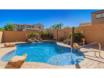 Backyard pool featuring waterfall and desert landscaping with blue handrail and brick patio at 20423 W Springfield St, Buckeye, AZ 85396