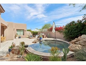Desert backyard features a stone-lined pool, patio seating, and a built-in grill at 7169 E Bramble Berry Ln, Scottsdale, AZ 85266
