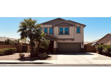 Two-story tan house featuring a two-car garage, desert landscaping, and palm trees at 41143 W Rio Bravo Dr, Maricopa, AZ 85138