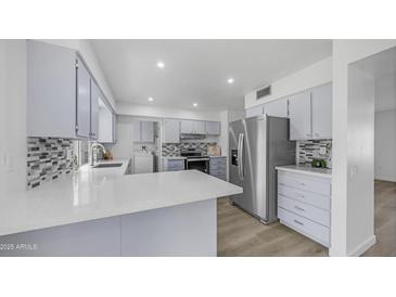 Renovated kitchen with stainless steel fridge, modern gray cabinetry, and sleek quartz countertops at 9911 W Pleasant Valley Rd, Sun City, AZ 85351