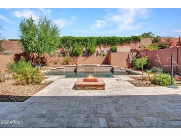 Inviting backyard oasis featuring a beautiful pool with a waterfall feature, a fire pit, and lush desert landscaping at 2462 W Turtle Hill Dr, Anthem, AZ 85086