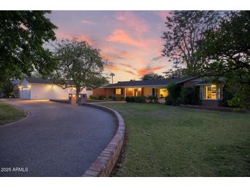 Charming single-story home with lush lawn, brick accents, and attached garage under a captivating sunset at 5818 N 3Rd Ave, Phoenix, AZ 85013