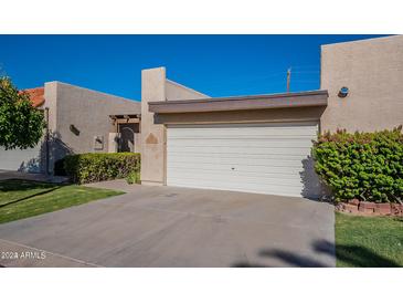 Attached two-car garage with a well-maintained desert landscape featuring mature shrubs and green grass at 3345 E University Dr # 72, Mesa, AZ 85213