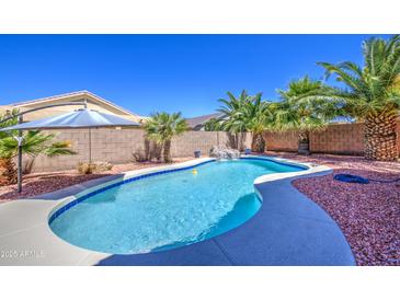 A private backyard oasis features a pristine pool, rock waterfall, and mature landscaping with palm trees at 43302 W Bunker Dr, Maricopa, AZ 85138