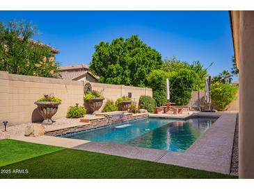 Beautiful backyard pool area with a small waterfall feature, lush greenery, and a relaxing patio space at 800 W Sycamore Ct, Litchfield Park, AZ 85340
