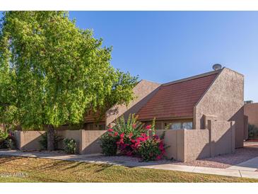 Charming home exterior featuring colorful bougainvillea, lush trees, and a private courtyard wall at 4317 W Orangewood Ave, Glendale, AZ 85301