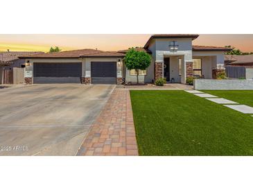 Charming single-story home featuring a well-manicured lawn, three-car garage, and neutral-toned facade with decorative stone accents at 4706 E Des Moines St, Mesa, AZ 85205