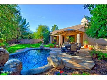 Inviting backyard featuring a sparkling pool with a rock waterfall and a patio with an umbrella table set at 1681 S Karen Dr, Chandler, AZ 85286