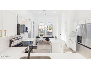 Bright modern kitchen featuring white cabinets, quartz countertops, stainless steel appliances, and an adjacent dining area at 7838 N 110 Ln, Glendale, AZ 85307