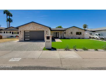 Charming single-story home featuring brick accents, lush green lawn, and modern garage door at 5425 E Avalon Dr, Phoenix, AZ 85018