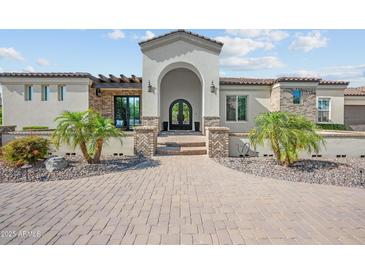 Stunning home with a large brick driveway, an arched entry, and beautiful landscaping with palm trees at 10448 E Glencove St, Mesa, AZ 85207