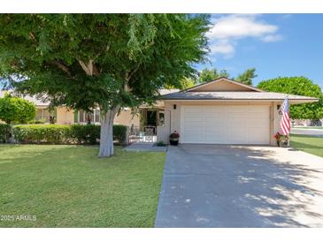 Charming home featuring a lush lawn, mature tree, and a two-car garage with an American flag at 17890 N 99Th Dr, Sun City, AZ 85373