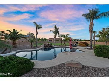 Stunning pool with rock waterfall feature, surrounded by lush landscaping and mature palm trees at sunset at 18822 E Flintlock Dr, Queen Creek, AZ 85142