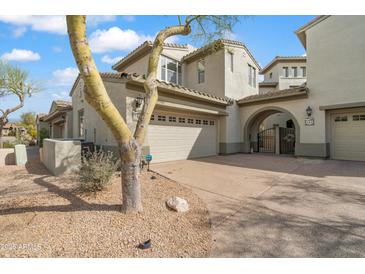 Inviting home exterior featuring desert landscaping, a two-car garage, and an arched entryway with gated access at 20802 N Grayhawk Dr # 1123, Scottsdale, AZ 85255