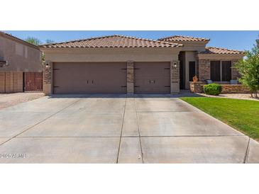 Inviting front view featuring a three car garage with brick accents, large driveway, and meticulously maintained landscaping at 20420 N 93Rd Dr, Peoria, AZ 85382