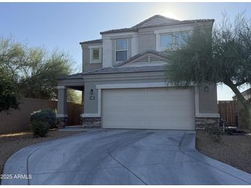 Two-story home featuring a two-car garage and a covered porch with stone accents. Landscaped with desert trees and bushes at 3402 N 300Th Dr, Buckeye, AZ 85396