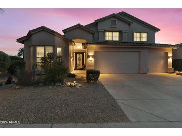 Charming home exterior with landscaped front yard and well-lit two-car garage beneath a picturesque twilight sky at 9517 E Minton St, Mesa, AZ 85207
