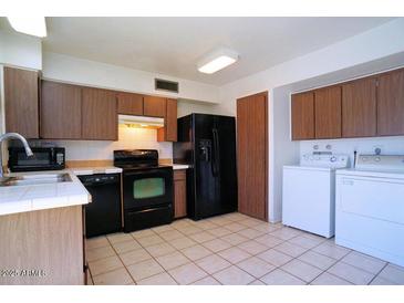 Cozy kitchen featuring tiled floors, brown cabinetry, and black appliances at 4625 W Thomas Rd # 71, Phoenix, AZ 85031