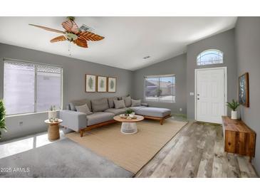 Bright living room featuring a large gray sofa, hardwood floors, and a decorative ceiling fan at 13416 W Ventura St, Surprise, AZ 85379