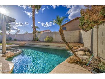 Backyard pool features palm trees, a rock waterfall, and ample space for relaxation and entertainment at 3834 E Windsong Dr, Phoenix, AZ 85048