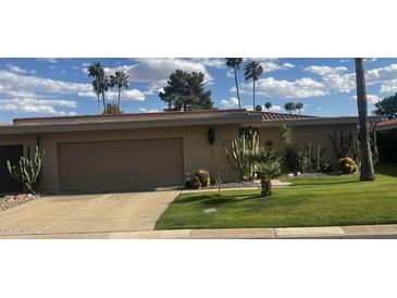 Charming home features a well-manicured lawn and desert landscaping with various cacti, palms, and a two car garage at 7615 E Tucson Rd, Scottsdale, AZ 85258