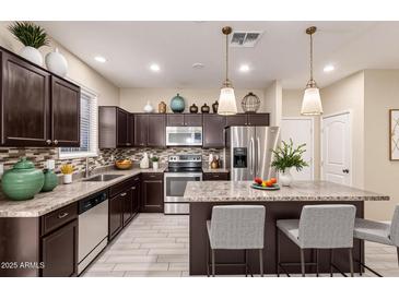 Modern kitchen features stainless steel appliances, dark wood cabinets, and a large island with seating at 7769 W Bonitos Dr, Phoenix, AZ 85035