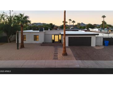 Inviting single-story home boasts desert landscaping, a brick driveway and desert mountain views at sunset at 3615 E Charter Oak Rd, Phoenix, AZ 85032