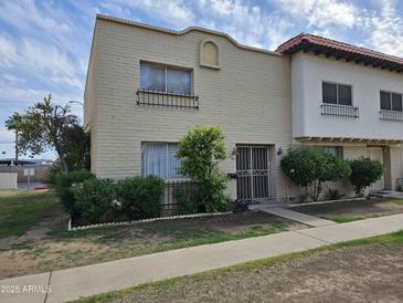 Beige stucco townhome showcasing lovely shrubbery and metal security doors at 4614 N 19 Ave, Phoenix, AZ 85015