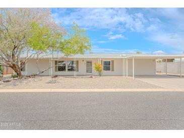 Inviting single-story home with a covered parking area and xeriscaped front yard featuring mature trees and desert plants at 16008 N 69Th Ln, Peoria, AZ 85382