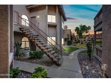 A well-maintained condo exterior features classic desert landscaping, with walkways and exterior stairs visible at sunset at 930 N Mesa Dr # 1079, Mesa, AZ 85201