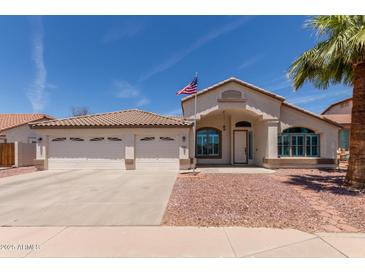 Charming single-story home featuring a three-car garage, desert landscaping, and American flag at 9566 E Plana Ave, Mesa, AZ 85212