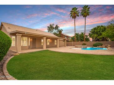 Resort style backyard with refreshing in-ground pool, rock waterfall, mature palm trees, lush lawn and covered patio at 1523 E Tulsa St, Chandler, AZ 85225