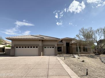 Tan home with a three car garage, a tile roof, and desert landscaping with rocks and native plants at 6931 E Teton Cir, Mesa, AZ 85207
