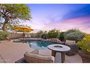 Backyard pool with a beautiful lounge area, complete with an umbrella and a fire pit, against a picturesque sky at 10623 E Acacia Dr, Scottsdale, AZ 85255