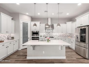 A bright kitchen boasts white cabinets, stainless appliances, a large island, and stylish backsplash at 10949 N 183Rd Dr, Surprise, AZ 85388