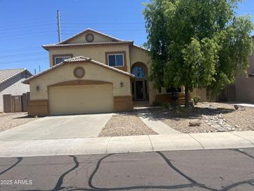 Charming two-story home with a tan stucco exterior, attached garage, landscaped yard, and inviting arched front door at 15897 N Gil Balcome St, Surprise, AZ 85374
