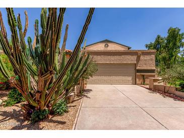 Beige home featuring a two-car garage and well-maintained desert landscaping, complete with various cacti and shrubbery at 630 E Jensen St # 102, Mesa, AZ 85203