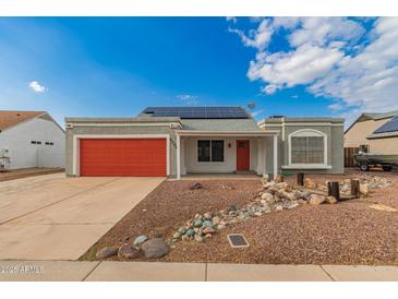 Charming single-story home showcasing desert landscaping, a red garage door, and solar panels under a bright sky at 6038 W Gelding Dr, Glendale, AZ 85306
