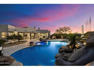Stunning backyard featuring a custom pool with rock accents and lush desert landscaping at dusk at 9022 E Diamond Rim Dr, Scottsdale, AZ 85255